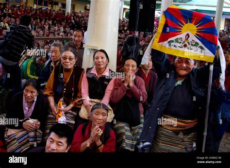 An Exiled Tibetan Woman Holds A Flag As She And Others Look On During