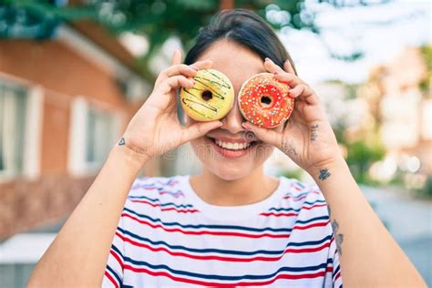 Jovencita Latina Sonriendo Feliz Sosteniendo Donuts Sobre Los Ojos Caminando Por La Ciudad