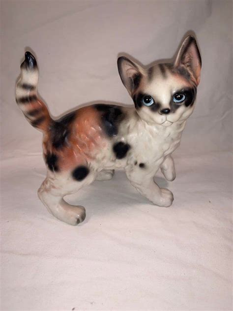 A Cat Figurine With Blue Eyes And Black Spots On Its Body