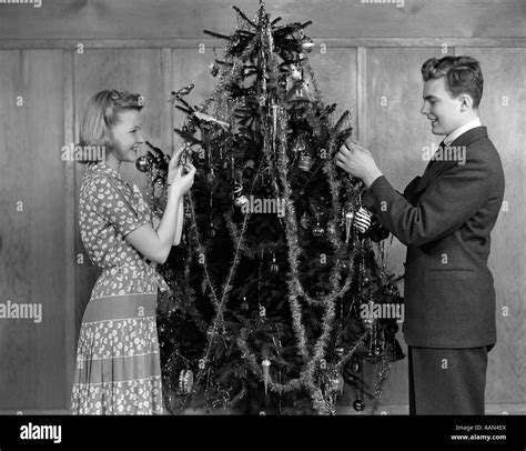 1940s Couple Decorating Christmas Tree With Tinsel And Ornaments Stock