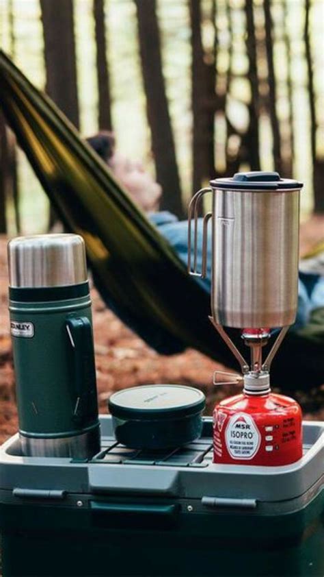 A Man Laying In A Hammock Next To A Camping Stove And Coffee Maker