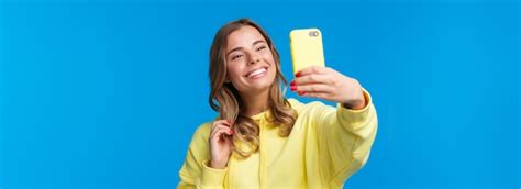 Closeup portrait tendre jolie fille blonde en sweat à capuche jaune tenant un téléphone mobile