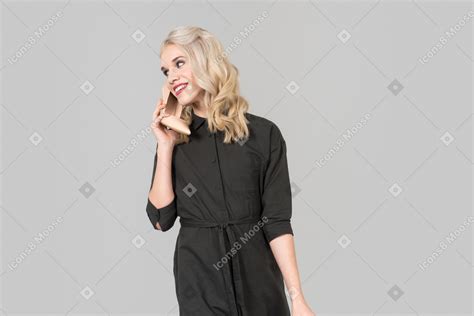 Eine junge blonde person in einem schwarzen kleid und beige high heels in ihren händen vor