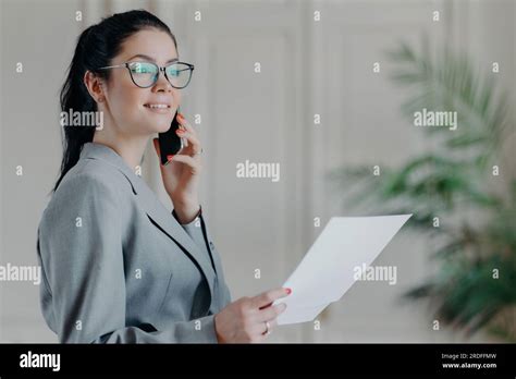 Elegant Brunette Manager In Formal Attire Handles Papers Discusses Business Via Smartphone