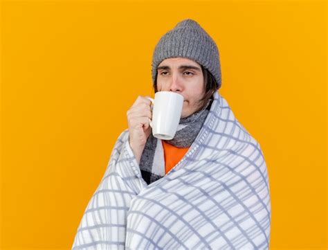 Débil joven enfermo con sombrero de invierno con bufanda bebiendo té