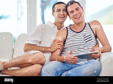 We Keep Each Other Laughing Portrait Of A Gay Couple Using A Digital Tablet While Relaxing On