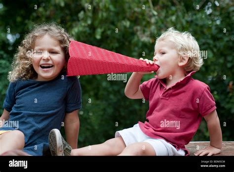 Two Young Children Talking And Laughing Using Homemade Megaphone Stock