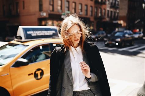 Une blonde en manteau noir se tient dans la rue ensoleillée quelque part dans la ville de New