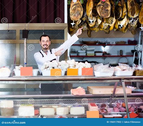 Young Man Shop Assistant Demonstrating Sorts Of Meat In Shop Stock