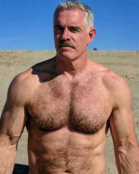 A Shirtless Man Standing In The Sand With His Hand On His Hip And