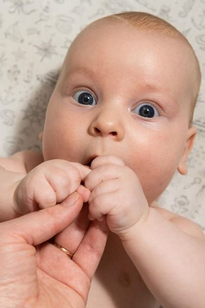 O bebê brinca e come as mãos e olha para a câmera Foto Premium