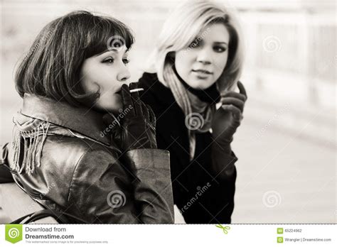 Duas Mulheres Novas Felizes Da Forma Que Fumam Um Cigarro Foto De Stock