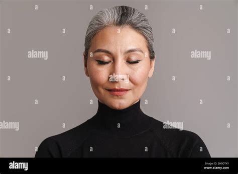 Mature Asian White Woman Posing With Her Eyes Closed Isolated Over Grey Background Stock Photo