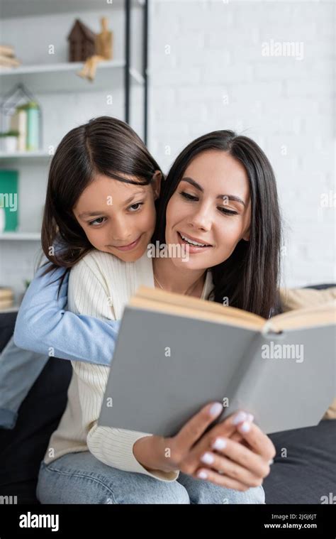 Smiling Girl Embracing Nanny Reading Book At Home Stock Photo Alamy