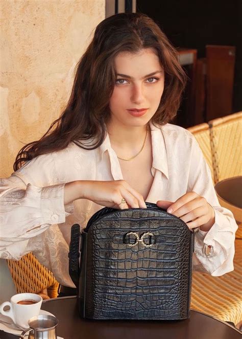 A Woman Sitting At A Table With A Purse In Front Of Her Holding It