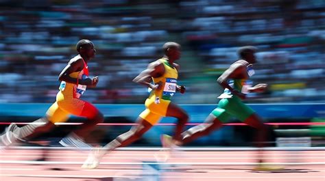 Three Men Running In A Race On A Track With A Crowd Watching Premium