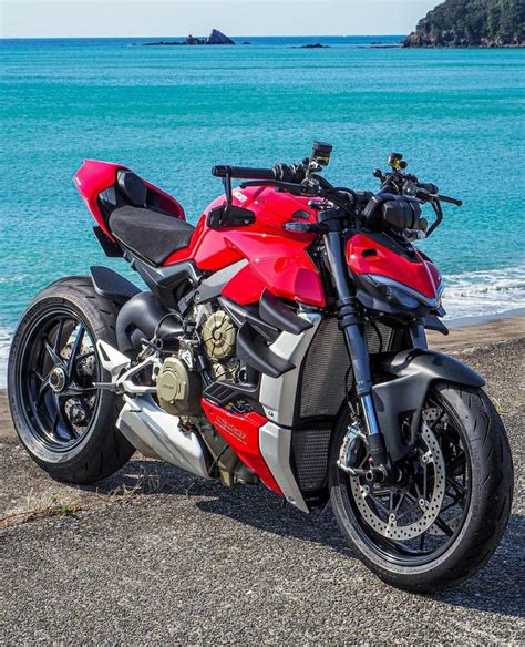 a red and black motorcycle parked on the side of a road next to the ocean