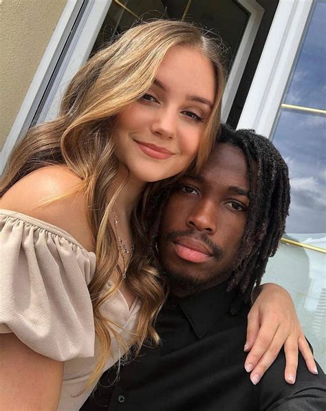 A Young Man And Woman Posing For A Photo In Front Of A Window With Their Arms Around Each Other