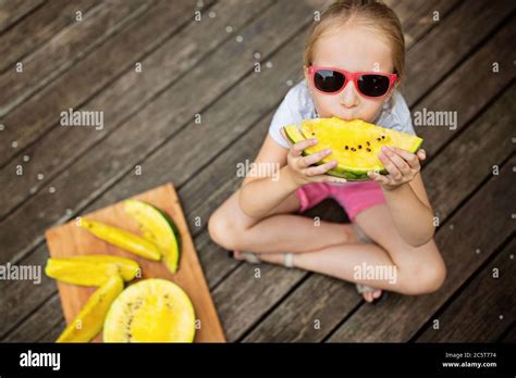 Bonne petite fille blonde assise à l extérieur sur un pont en bois et mangeant de la pastèque