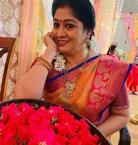 A Woman Sitting At A Table With Red Flowers In Front Of Her And Posing