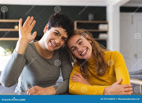 Happy Biracial Lesbian Couple Sitting At Home Having Video Call Waving