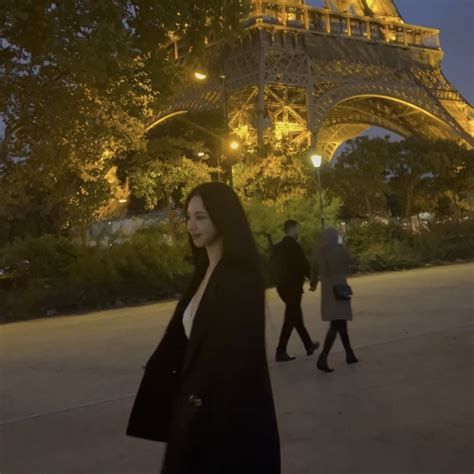 A Woman Walking In Front Of The Eiffel Tower At Night With People