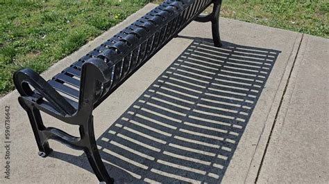 Metal park bench outside on sunny day with shadow pattern on concrete ...