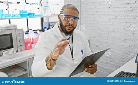 Professional Black Man In Lab Coat Holding A Clipboard In A Modern