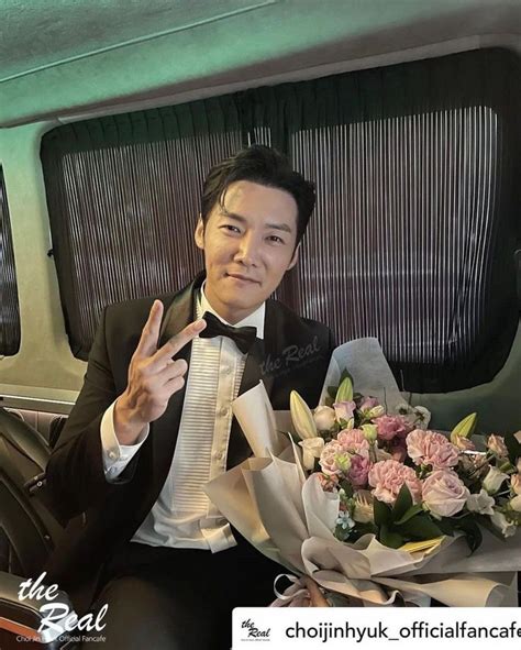 A Man In A Tuxedo Holding Flowers And Giving The Peace Sign With His Hand