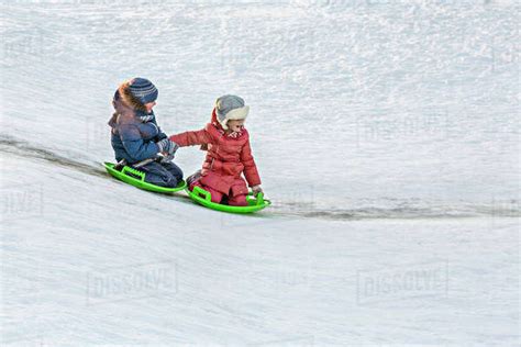 Full Length Of Siblings Tobogganing Together In Snow Stock Photo