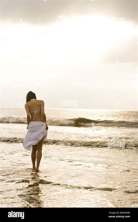Vue arrière du jeune femme en bikini blanc et jupe en marche à la plage de l océan Photo Stock