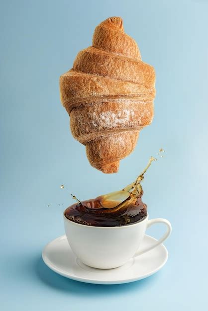 Premium Photo A Cup Of Coffee And A Levitating Croissant On A Blue