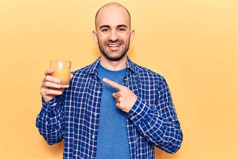 Young Handsome Bald Man Drinking Glass Of Healthy Orange Juice Smiling