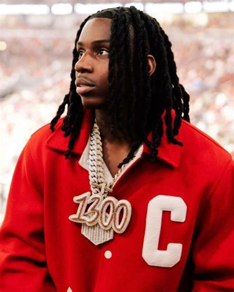 A Man With Dreadlocks Standing In Front Of A Crowd Wearing A Red Jacket