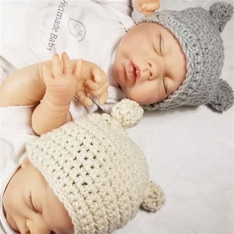 a baby wearing a crocheted hat and sleeping next to a teddy bear toy