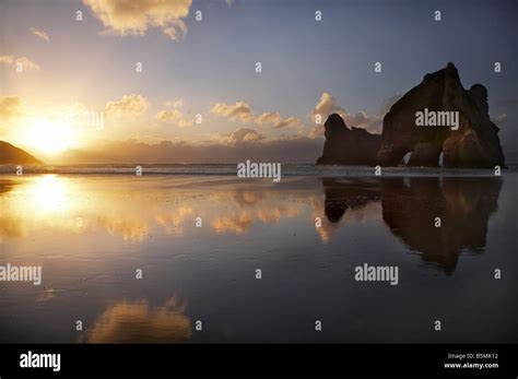 Archway Islands Reflected In Wet Sands Of Wharariki Beach At Sunset