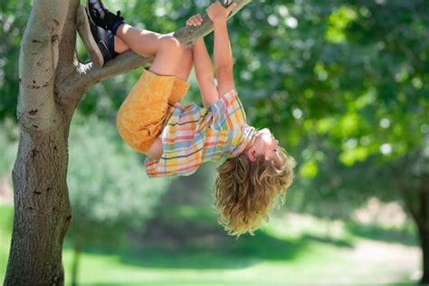 Niño jugando y trepando a un árbol y colgando de una rama Foto Premium