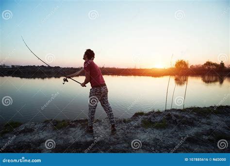 Young Man Fishing On A Lake At Sunset And Enjoying Hobby Stock Photo