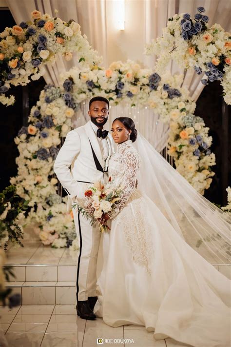 A Bride And Groom Posing For A Photo In Front Of A Floral Arch At Their