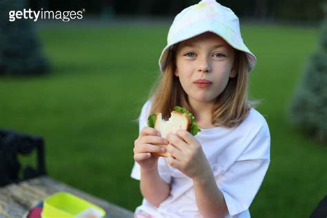 A Cute Schoolgirl Eating A Sandwich On A Park Bench She Is A Cheerful Pupil Enjoying Her Lunch