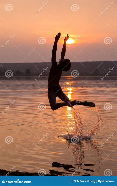 El Muchacho Que Salta En El Agua En Puesta Del Sol Imagen De Archivo