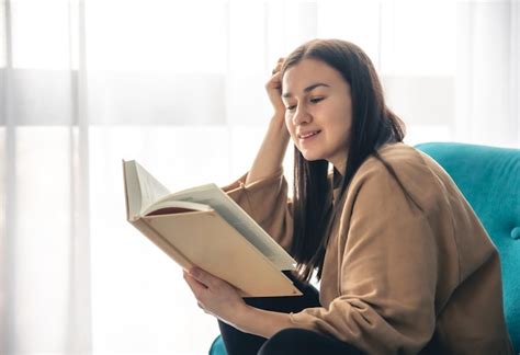 Una Mujer Joven Est Leyendo Un Libro Sentada En Un Sill N Junto A La