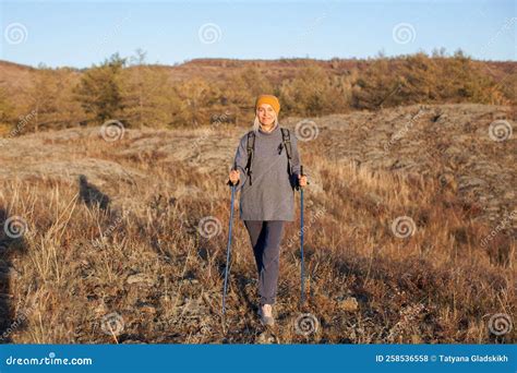 Attractive Middle Aged Woman In Activewear Hiking In Forest Using Poles