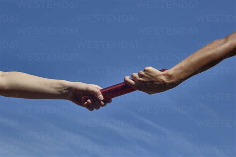 Hands Of Female Relay Runners Passing Baton Against Blue Sky Stock Photo