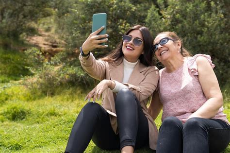 Una joven adulta latina y su madre sentadas en el césped se están tomando una selfie Foto Premium