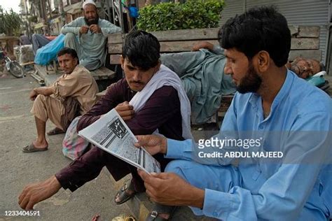 Daily Wage Labourers Sit Along The Roadside And Read A Newspaper As