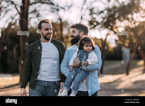 Male Gay Couple Walk In The Park In Love With Their Daughter In Their