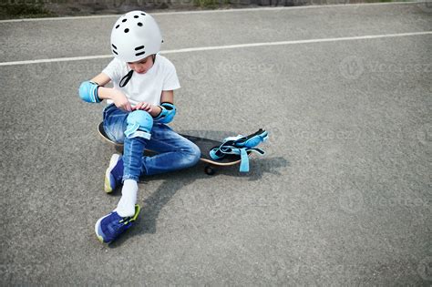 Front View Of A Sporty Boy In Safety Helmet Sitting On Skateboard And