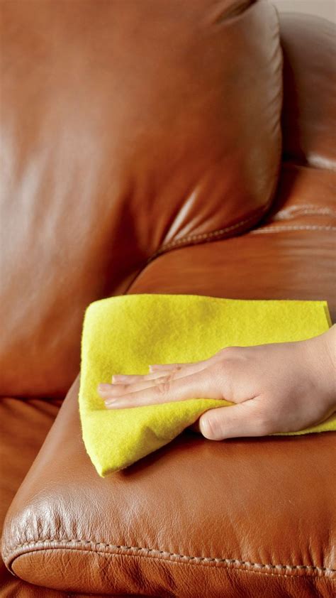 A Person Cleaning A Brown Leather Couch With A Yellow Micro Towel