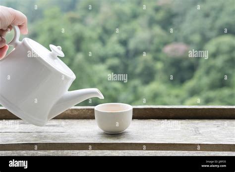 Woman S Hand Holding Teapot And Pouring White Tea Into Cup With Green